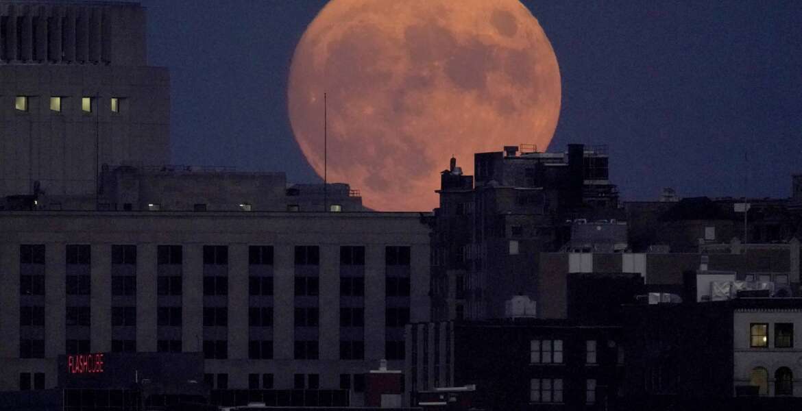The full harvest moon rises behind downtown buildings, Friday, Sept. 9, 2022, in Kansas City, Mo. (AP Photo/Charlie Riedel)